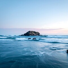 Calm ocean waters flow around a small rocky island under a soft dusk sky