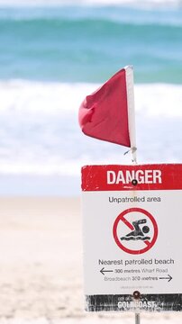 Red Danger Sign and Warning Flag on a Sunny Beach Shoreline