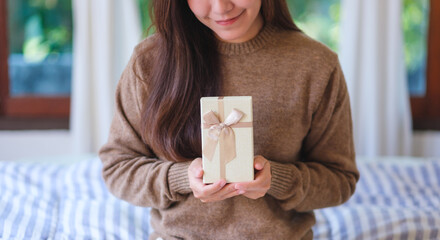 Closeup image of a woman in sweater holding a present box at home