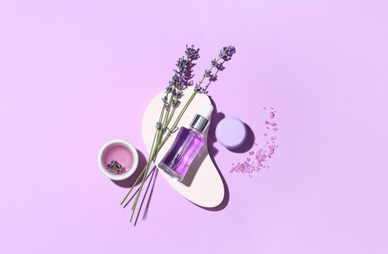 Plaster stand, jar of cosmetic product, bottle and bowl of lavender essential oil on lilac background