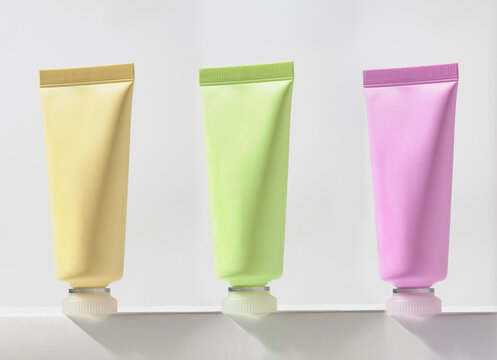 Set of three colorful, pastel-toned tubes in yellow, green, and pink, arranged in a row on a white podium, moderm abstract image for cosmetic brands and blog