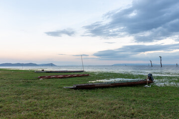 A serene summer sunset reflects across the blue water as fishing boats rest by the pier and bridge along the scenic river, lake, and sandy ocean beach shore