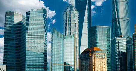 Modern glass skyscrapers with historic golden building during daytime under bright blue sky with white clouds, showing contrast between contemporary and heritage architecture