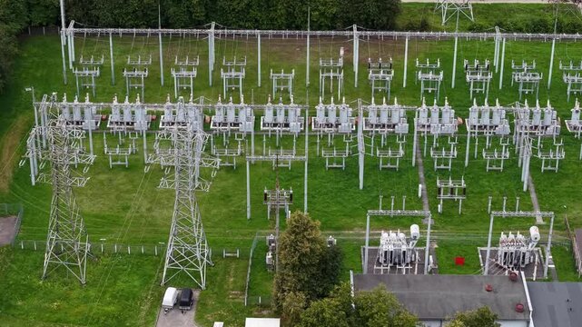 Aerial view of a high-voltage electrical substation with transformers, switchgear and steel pylons on green grass, showing modern electricity infrastructure and grid operations.