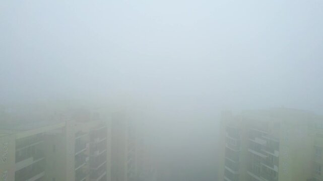 Aerial drone shot flying forward over buildings hidden in dense fog air pollution of Indian capital Delhi in severe winter prompting an emergency