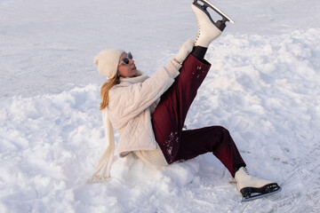 Flexible woman demonstrating stretching flexibility and split position on ice rink wearing figure skates beige jacket and burgundy pants in stylish winter athletic pose