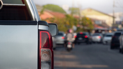 Close-up rear side of silver pickup car driving on the road. Drive through the long line of cars stuck in traffic around the bend in the road. With city and tree for background at day.
