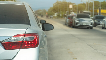 Rear side of silver car with turn on brake light on concrete road. Cars are parked waiting at the traffic light on the opposite side, despite the clear traffic conditions.