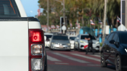 Rear side of pickup car with turn on brake light. Stop to let pedestrians cross at the red and white crosswalk. Were many cars parked in a row on the opposite road. Traffic in Thailand is like that.