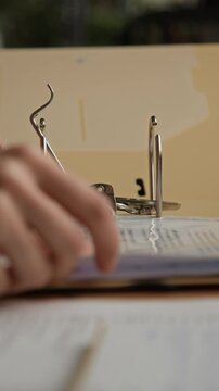Vertical close up of unrecognizable office employee using stapler to fasten paper documents while organizing paperwork at wooden desk in modern office environment