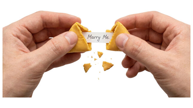 Two male hands breaking open a fortune cookie with a romantic marriage proposal message inside saying Marry Me, symbolizing a surprise engagement and commitment