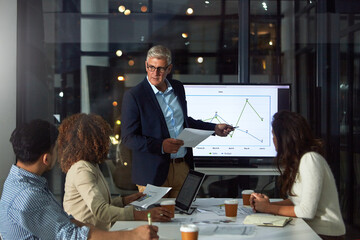 People, presentation and document in office at night with finance report, data analysis and profit. Mature man, team and paperwork with sales growth, audit graphs and overtime for performance metrics © BuyoutReese06/peopleimages.com