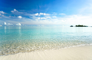 Soft ocean wave reaching a pristine white sand beach in the Maldives under a bright blue sky. A peaceful and luxury nature escape in a tropical paradise.