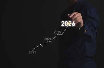 Business growth chart showing upward trend and year 2026 projection on hand. A futuristic business timeline concept moving from 2023 to 2026.