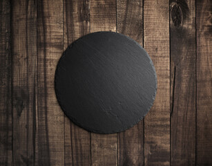 Blank black round stone slate plate on wooden textured surface. Copy space. Flat lay.