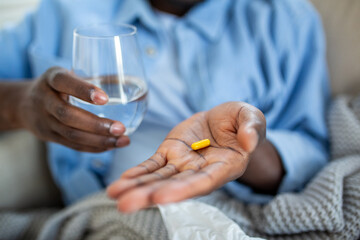 Close Up of African American Man Holding Yellow Medicine Capsule and Glass of Water, Black Male Hand with Prescription Pill for Pain Relief or Supplementation, Healthcare and Medical Concept