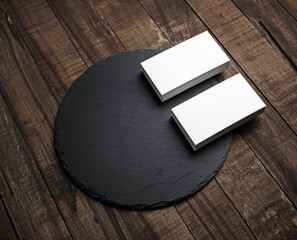 Two stacks of blank business cards and blank black round slate plate wooden textured surface. Template for ID.
