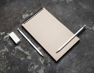 Closed blank kraft notebook, pencils and eraser on concrete surface. Stationery template.