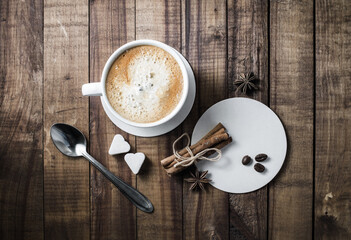 Coffee and spices. Coffee cup with cinnamon sticks, coffee beans, anise, sugar, spoon and coasters on wooden surface. Top view.