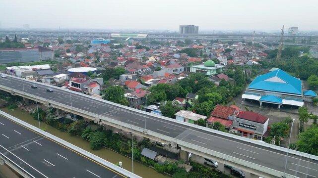 Aerial view of a modern highway cutting through dense housing, showing urban growth, transport flow, and city infrastructure in daylight.