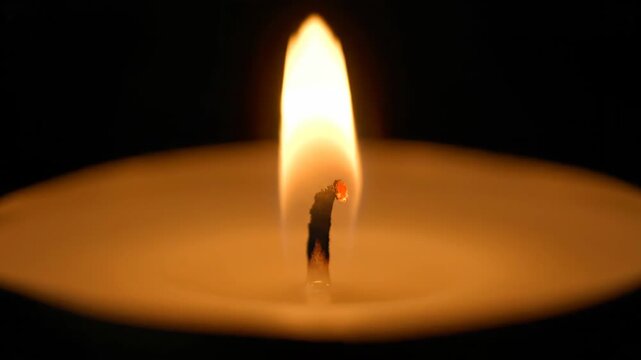 A single candle flame flickers gently in the darkness The warm orange light illuminates a tranquil scene creating a sense of peace and reflection