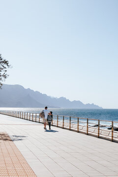 Father and child walking along seaside promenade with ocean and mount