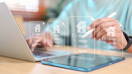 Person using stylus on tablet with virtual real estate documents and house icons. Concept of digital property management, e-signature, online contract, and smart real estate technology.