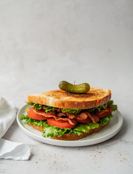 Freshly made BLT sandwich on plate with white backdrop.