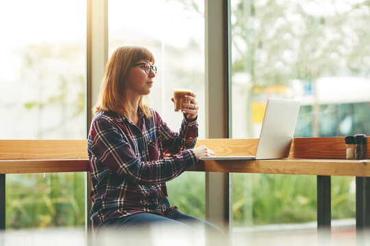 Woman, coffee and reading in cafe with laptop, remote work and online news report for journalism. Creative, person and freelance writer in restaurant with computer, hot drink and review for article.