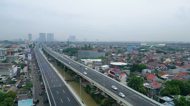Aerial view of a modern highway cutting through dense housing, showing urban growth, transport flow, and city infrastructure in daylight.