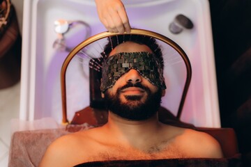 Man receiving professional relaxing water head massage with jade mask