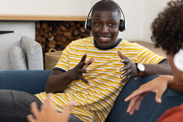 Naklejka premium Diverse friends chatting using over-ear headphones while sitting on fabric sofa in living room