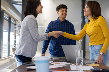 Obraz premium Diverse coworkers shaking hands across conference table in office around laptop and coffee