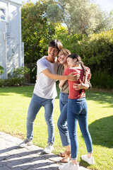 Diverse family hugging each other on stone pathway in backyard garden under bright sunshine