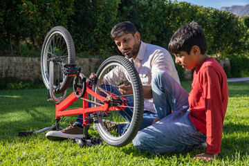 Indian father with son kneeling on suburban lawn repairing red bicycle using wrench and toolkit © wavebreak3