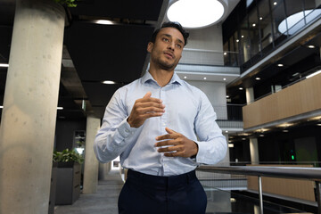 Businessman wearing suit standing next to glass and metal railing overlooking floor in office