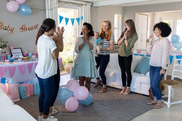 Obraz premium Diverse female friends applauding pregnant friend around baby shower table at home, cupcakes