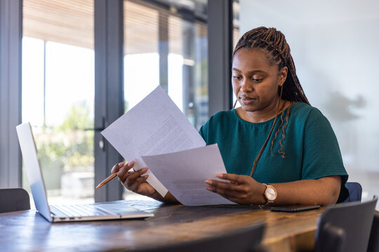 Woman reviewing documents with copper pen beside laptop at office desk, copy space
