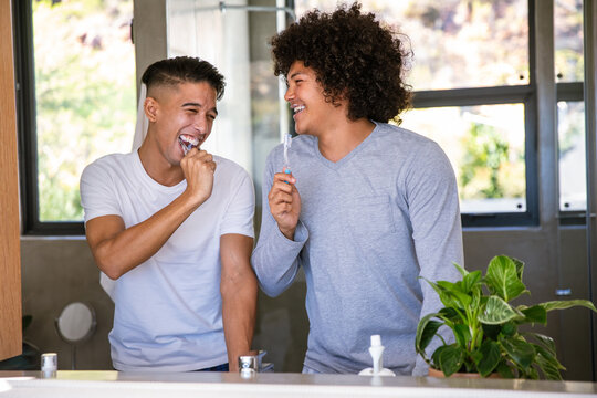 Diverse male friends brushing teeth while laughing at bathroom sink with toothbrushes