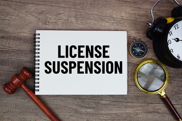 License Suspension message written on notepad with alarm clock, wood gavel and magnifying glass flat lay on wooden background