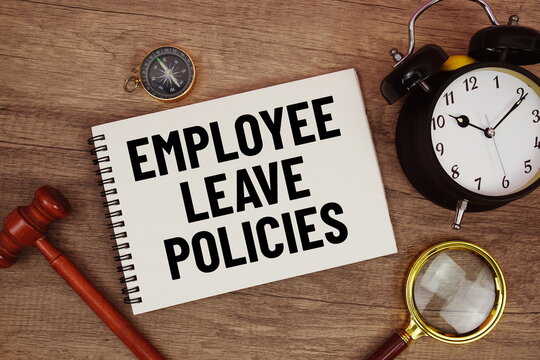 Employee Leave Policies message written on notepad with alarm clock, wood gavel and magnifying glass flat lay on wooden background