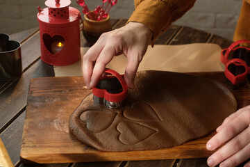 Making cookies for St. Valentines Day. Hand cutting heart shaped figures out of rolled dough