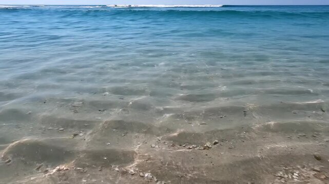 Crystal clear ocean water shimmers with sunlight dancing on the sandy seabed Gentle waves lap the shore under a bright blue sky
