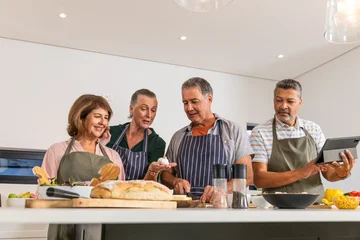 Selbstklebende Fototapeten Zu Kochen Diverse senior friends chopping vegetables and arranging ingredients on kitchen island under lights  © wavebreak3