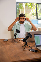 Indian man preparing podcast and adjusting headphones, microphones, laptop, smartphone at home © wavebreak3