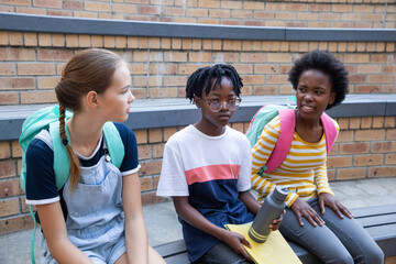 Diverse child classmates sitting on bleachers with backpacks holding water bottle notebook
