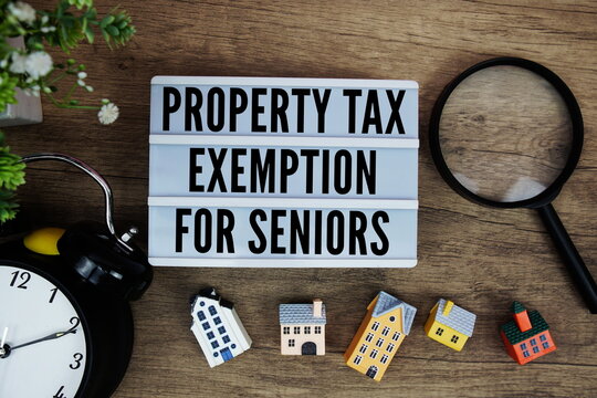 Property Tax Exemption For Seniors text in lightbox with house model, magnifying glass and alarm clock on wooden background