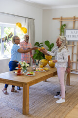 Diverse senior friends toasting juice glasses at dining table with retirement banner