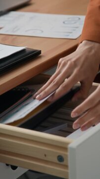 Vertical close up of unrecognizable office worker tapping pen on wooden desk while handling documents and paperwork at workplace during focused office task