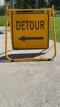 yellow detour sign on metal frame outdoors on footpath